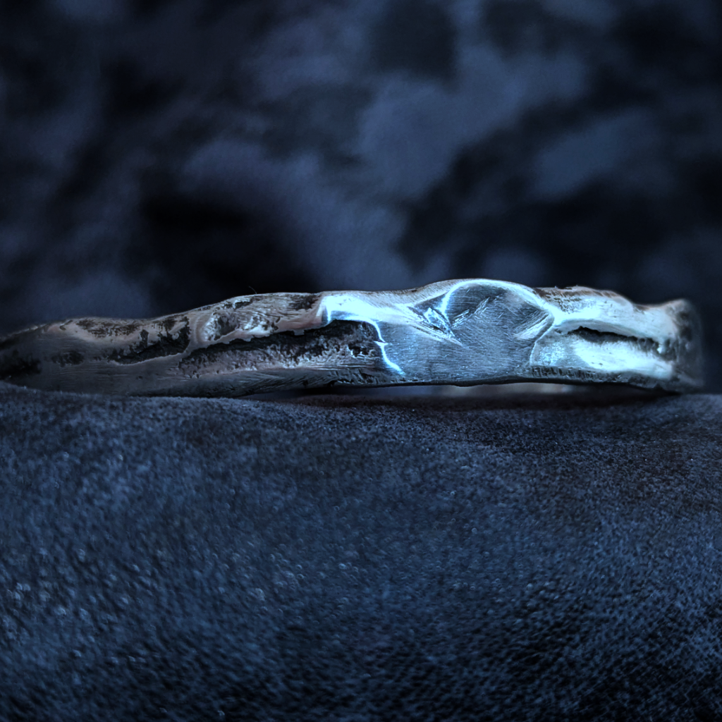 Découvrez ce bracelet jonc en argent massif 925 à la patine noire unique. Une pièce texturée et organique, fabriquée à la main en Corse. Design brut et élégant.
